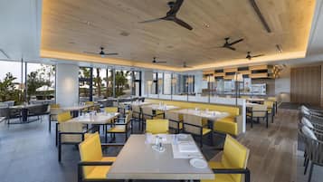 Un restaurant moderne doté de nombreuses tables et chaises, de ventilateurs de plafond et de grandes fenêtres.