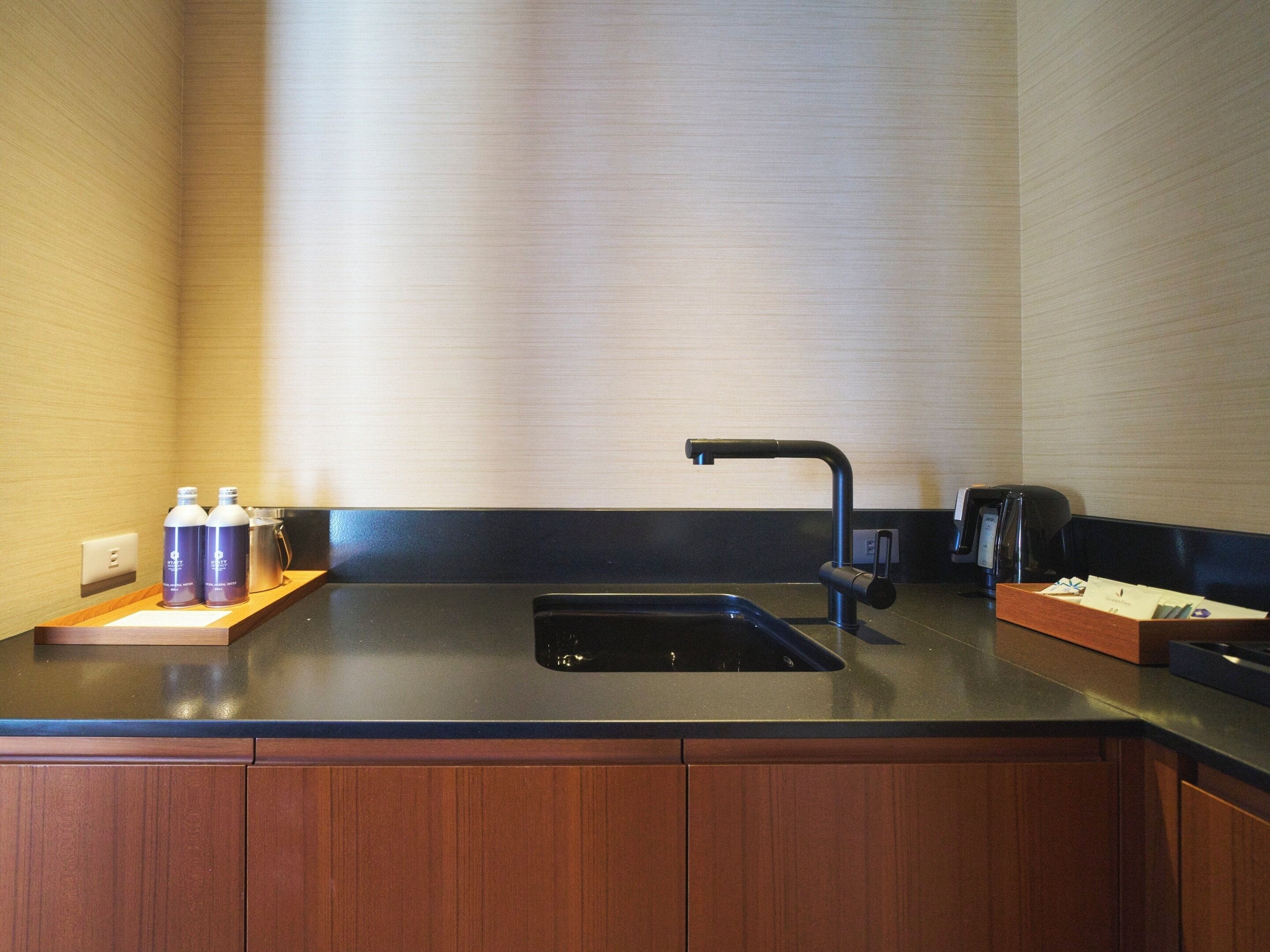 A modern kitchen with a black sink, a coffee maker, and two water bottles on a wooden counter.