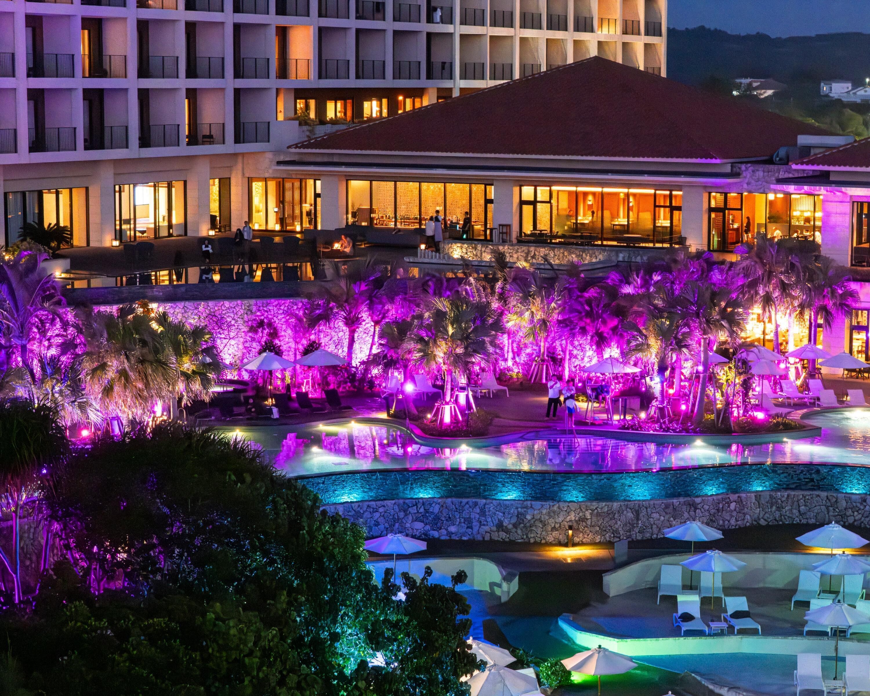 A hotel with a pool area, multiple floors, and a well-lit facade.