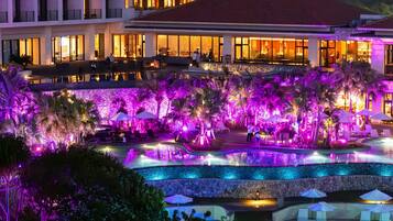 A hotel with a pool area, multiple floors, and a well-lit facade.
