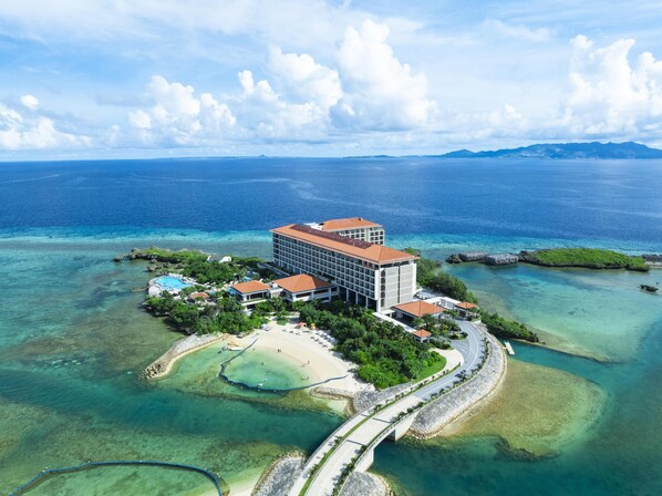 An aerial view of a resort with a large building, multiple smaller structures, a beach, and clear blue waters.