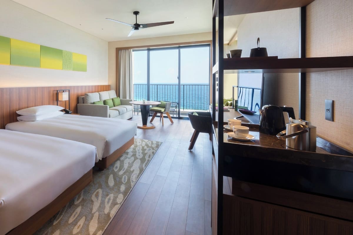 A hotel room with two beds, a balcony with a view, a dining area, and a TV.