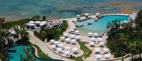 A resort with a large pool, sun loungers, umbrellas, and a view of the ocean.