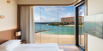 Habitación de hotel con un gran ventanal corredera que da a una vista de la playa, una cama y un televisor.