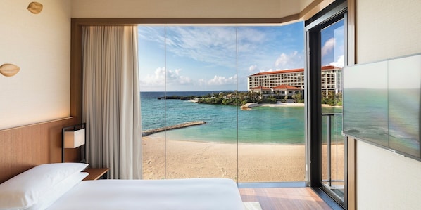 Een hotelkamer met een grote glazen schuifdeur naar uitzicht op het strand, een bed en een televisie.