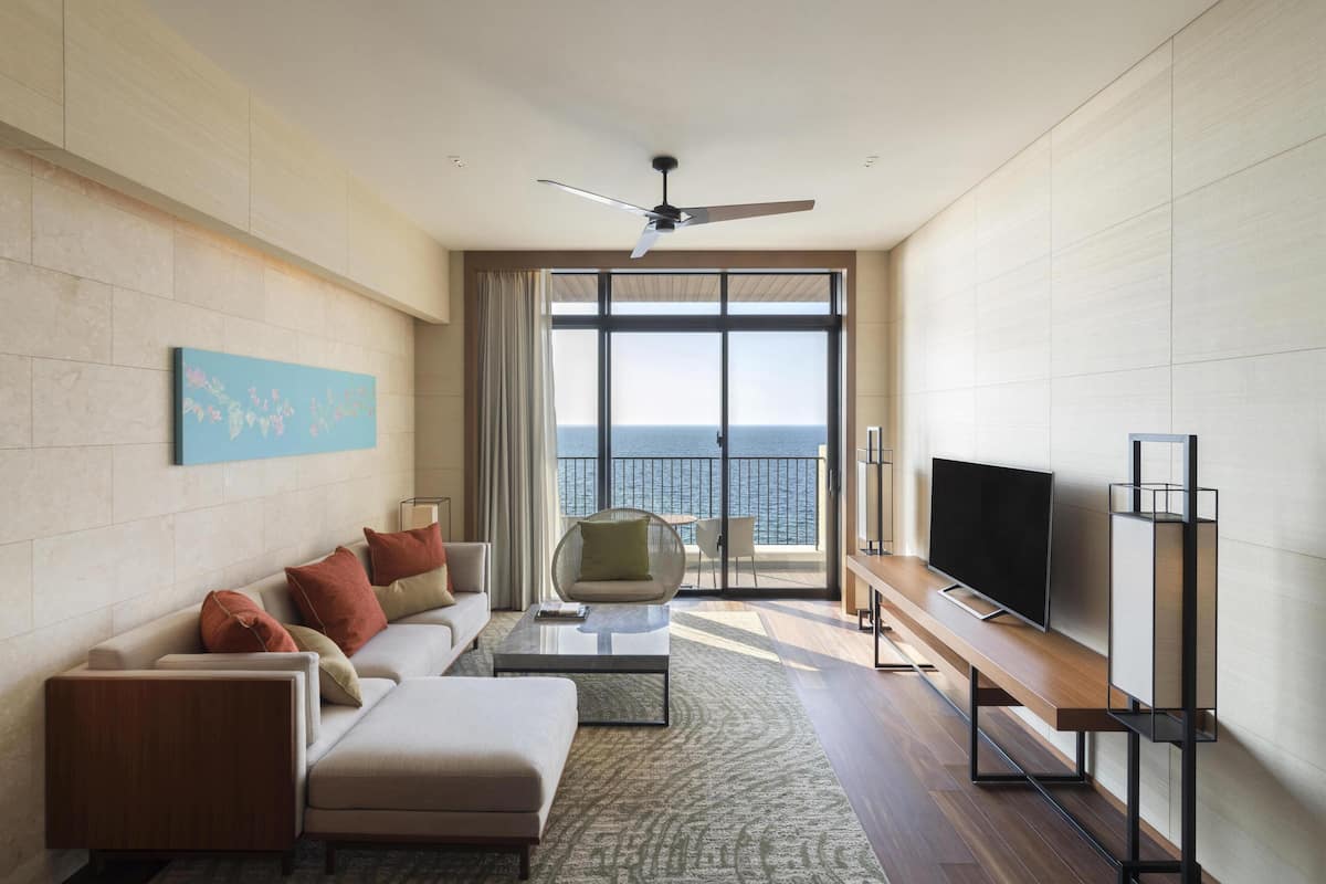 A modern living room with a sofa, coffee table, TV, and a balcony with a view of the sea.