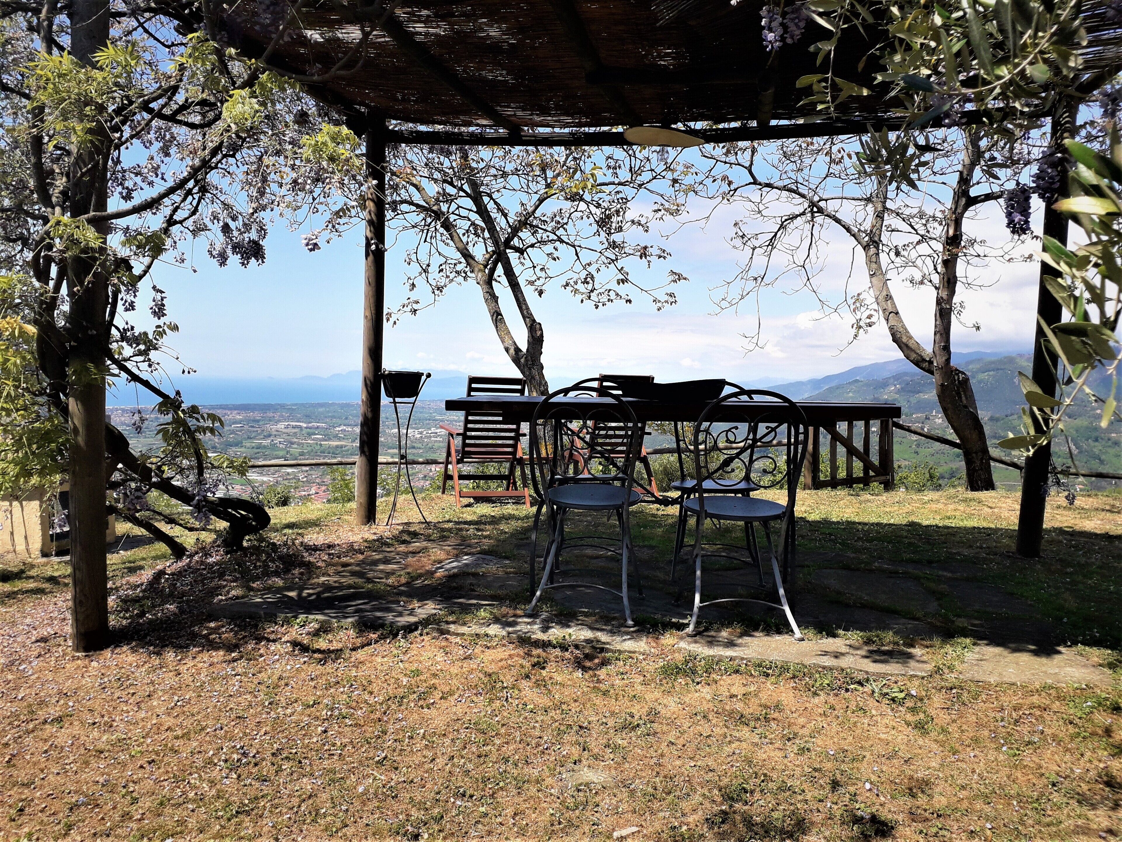 An outdoor seating area with a table and chairs under a pergola, overlooking a scenic view of a valley and mountains.