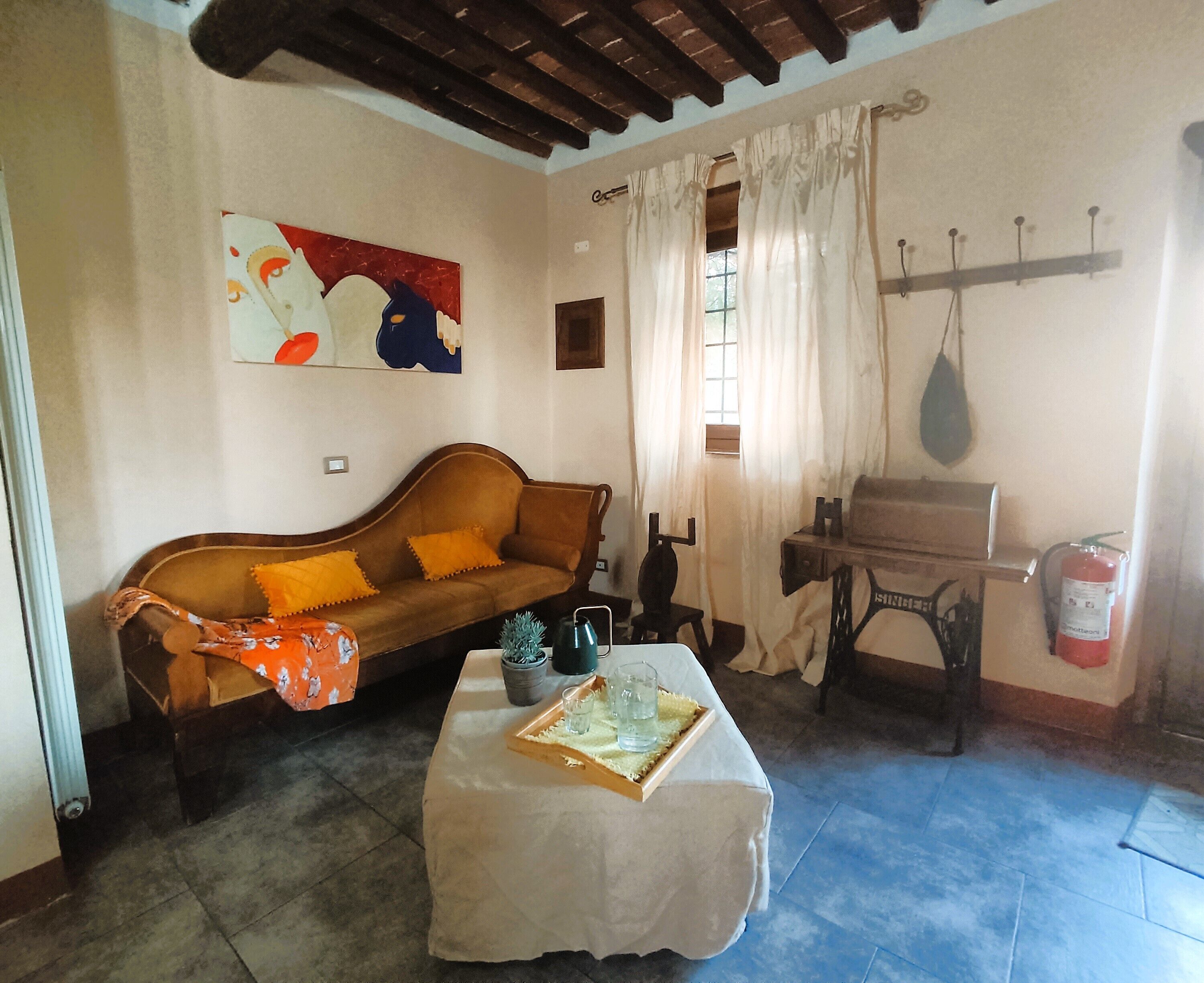 A cozy living room with a sofa, a table with a tray of glasses, a sewing machine, and a fire extinguisher.