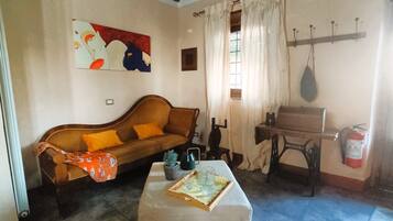 A cozy living room with a sofa, a table with a tray of glasses, a sewing machine, and a fire extinguisher.