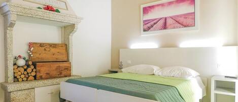 A bedroom with a bed, a nightstand, a wooden chest, and a fireplace.
