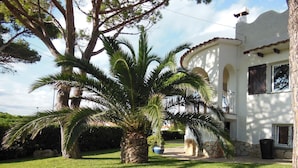 A white building with a stone base and arched windows, surrounded by a well-maintained lawn and palm trees. - Villa in L'Escala, Costa Brava, Spain. - Private Pool (L'Escala)
