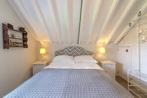 A bedroom with a bed, two bedside tables, a wall-mounted shelf, and a door.