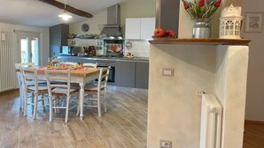 A kitchen with a wooden table and chairs, a refrigerator, and a shelf with flowers. - Luminosa e caratteristica mansarda con affacci su Villa Bottini in centro conA/C (Lucca)