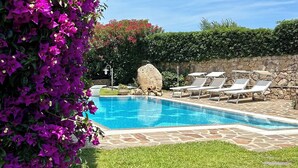A swimming pool with lounge chairs, surrounded by green grass and purple flowers.
