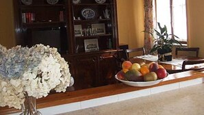 Comedor con una mesa de madera, un frutero, una planta en maceta y una estantería con platos.