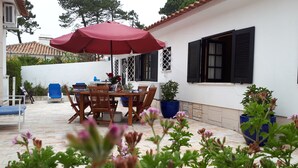 Un patio al aire libre con una mesa y sillas de madera, un paraguas rojo y plantas en macetas.