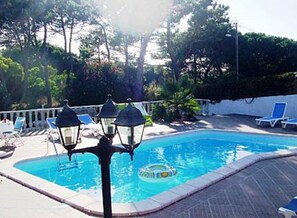 Une piscine entourée d’arbres et d’une clôture blanche, avec des chaises longues et un flotteur.