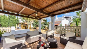 An outdoor patio with wicker furniture, a table with a bottle and glasses, and a view of the surrounding area including buildings and greenery.