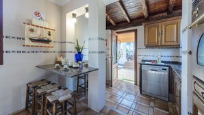 A kitchen with a tiled backsplash, wooden bar stools, a blue vase, and a dishwasher.