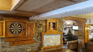 A cozy room with a dartboard, a wooden cabinet, a stone wall, and a Christmas tree. - Hotel Martin (Sauze d'Oulx)
