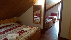 Un dormitorio con techo inclinado, una cama de madera, un espejo y otra cama al fondo.