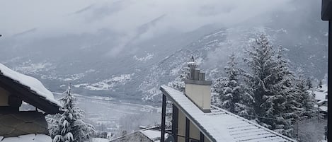 Un paisaje montañoso nevado con una casa con techo inclinado y chimenea.