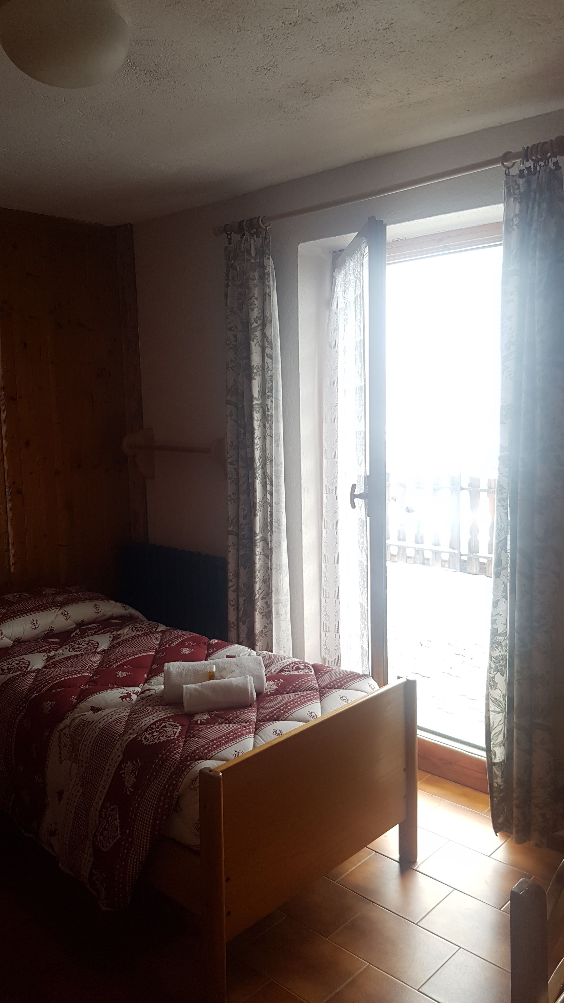 A bedroom with a wooden bed, a window with curtains, and a view of the outside.
