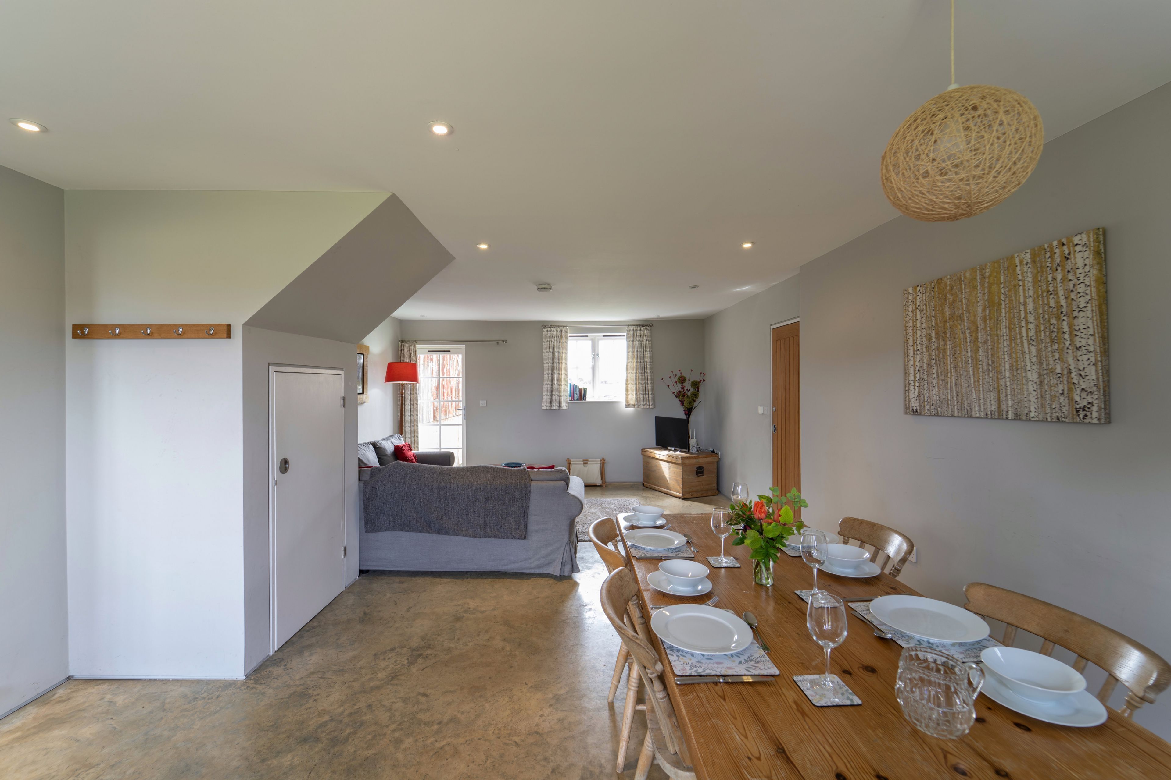 Een eetgedeelte met een houten tafel voor vier personen, een bankstel op de achtergrond en een keuken die zichtbaar is door een open deur.