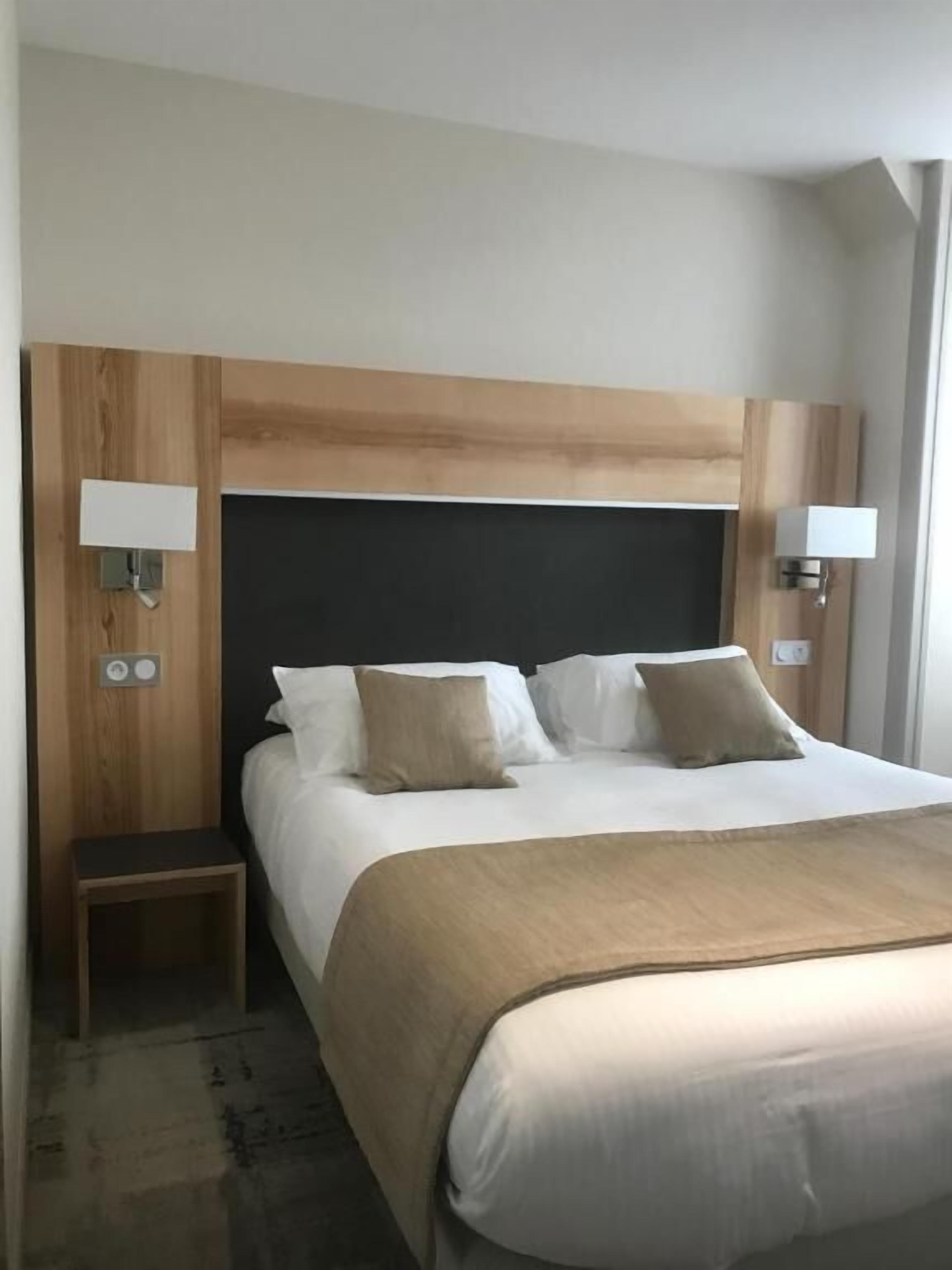 A hotel room with a large bed, wooden headboard, two bedside tables, and wall-mounted lamps.