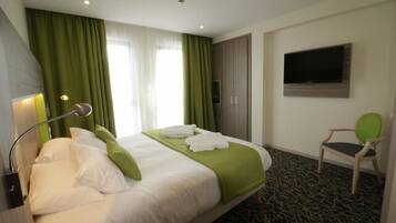 A hotel room with a bed, green curtains, a TV mounted on the wall, and a chair.