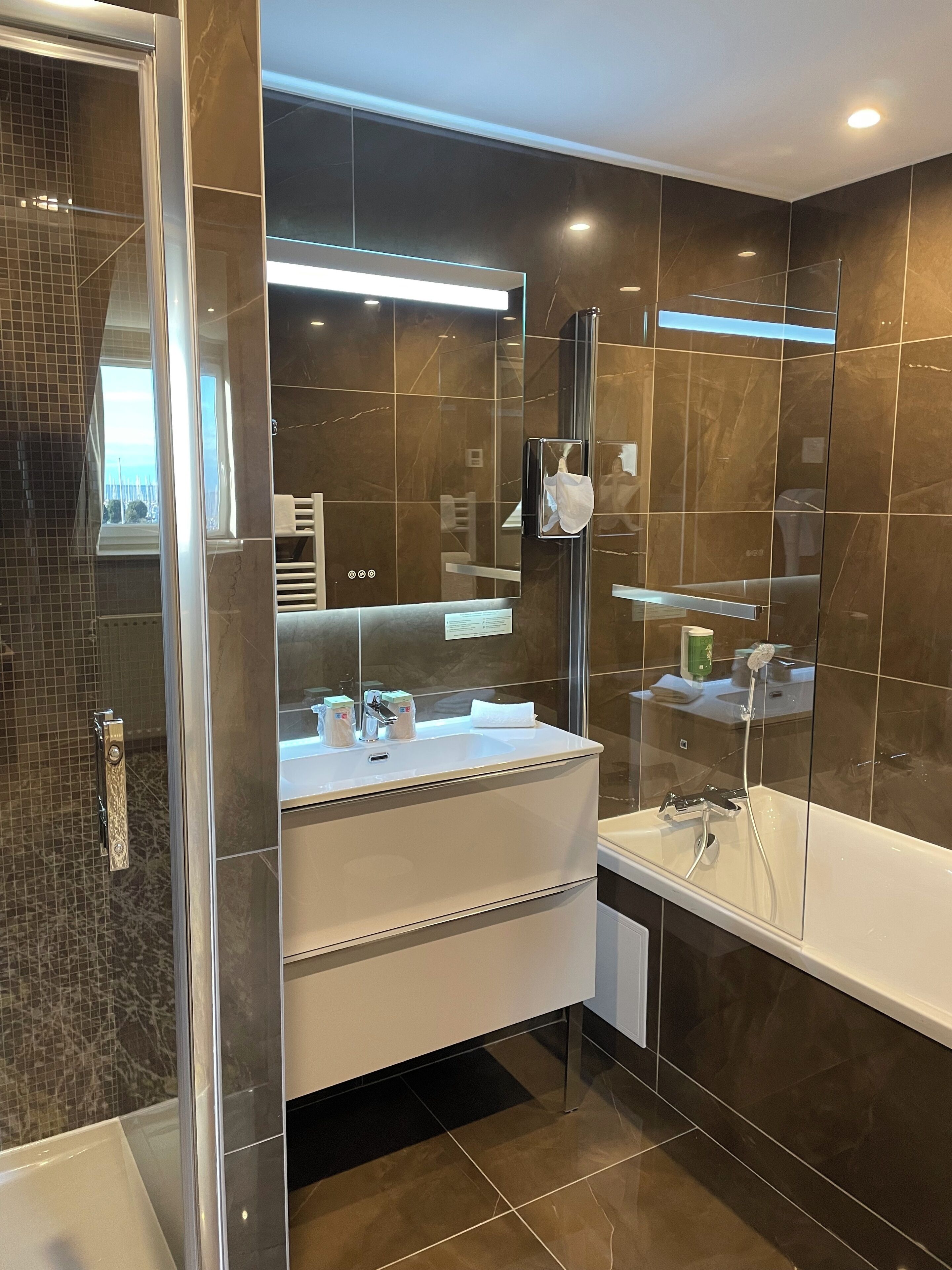 A modern bathroom with a glass-enclosed shower, a white sink with a mirror above, and a large mirror on the wall.