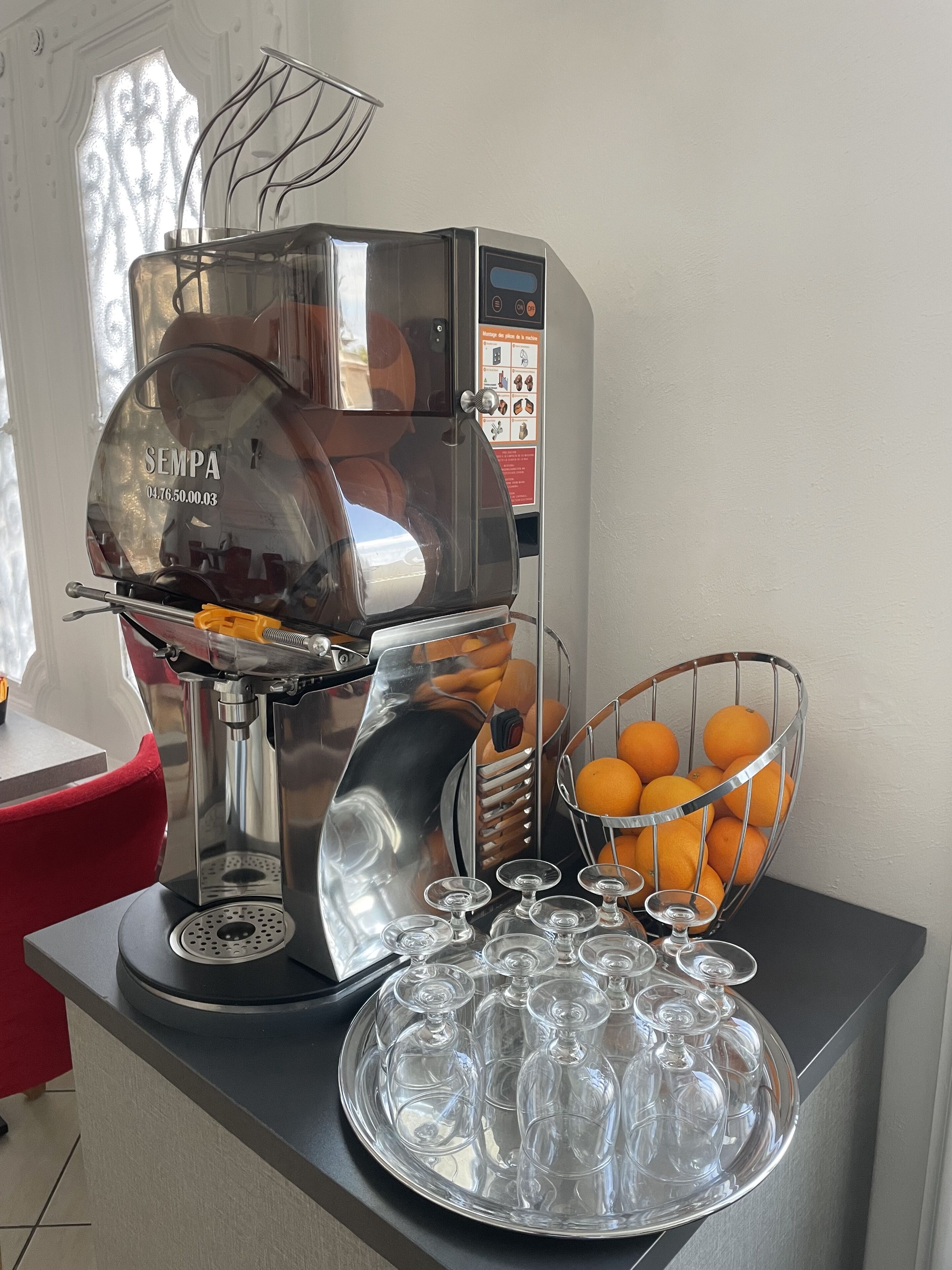 A coffee machine with a glass carafe and a bowl of oranges on a table.