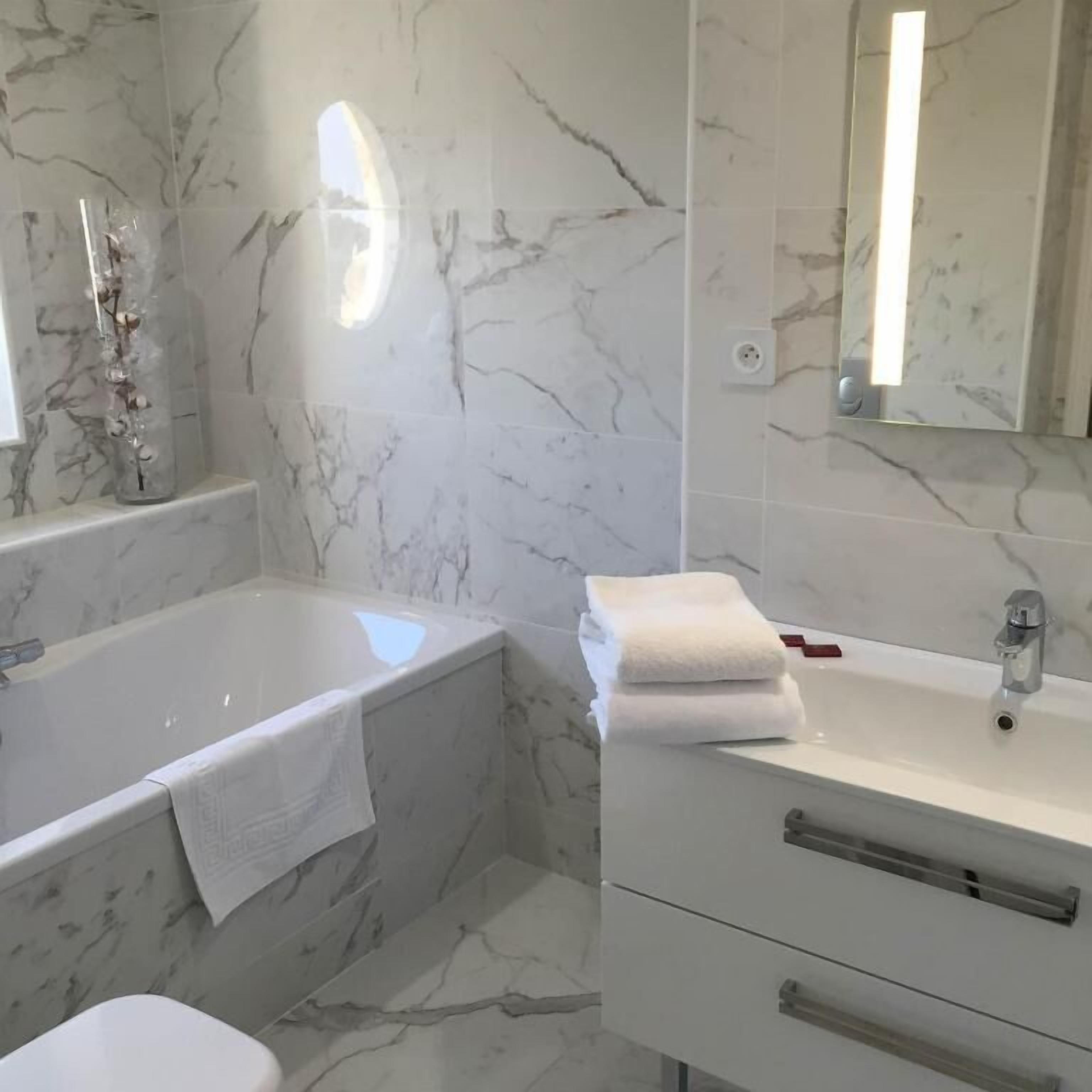 A bathroom with a marble floor, a bathtub, a sink with a mirror, and a toilet.
