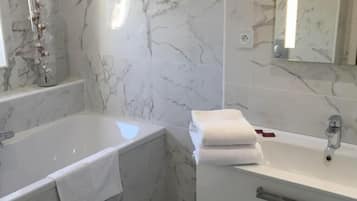 A bathroom with a marble floor, a bathtub, a sink with a mirror, and a toilet.