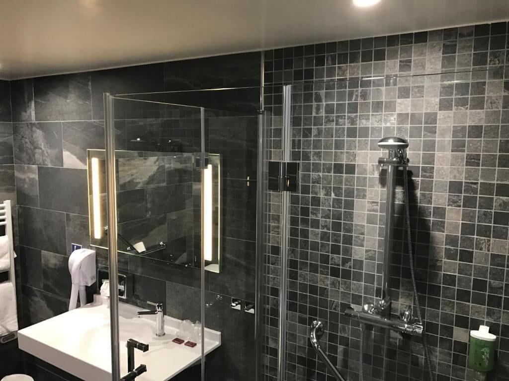 A modern bathroom with a glass-enclosed shower, a white sink, and a large mirror.