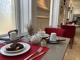 Una mesa de comedor dispuesta con un plato de pastel de chocolate, una tetera, tazas y un bol pequeño de fruta.