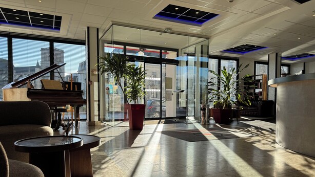 Een ruime lobby met een vleugelpiano, comfortabele zitplaatsen en grote ramen met uitzicht op de stad.