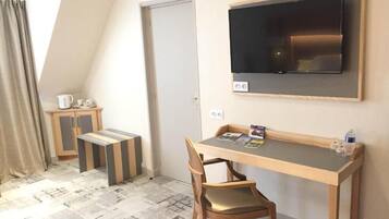 Een kleine kamer met een bureau, stoel en een aan de muur bevestigde televisie.