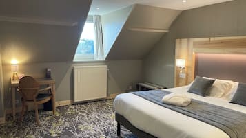 Une chambre d’hôtel avec un lit, un bureau, une chaise, un radiateur et une fenêtre avec des rideaux.