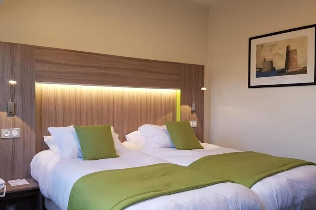 Quarto de hotel com uma cama grande, dois travesseiros, mesa de cabeceira com telefone e luminária na parede.
