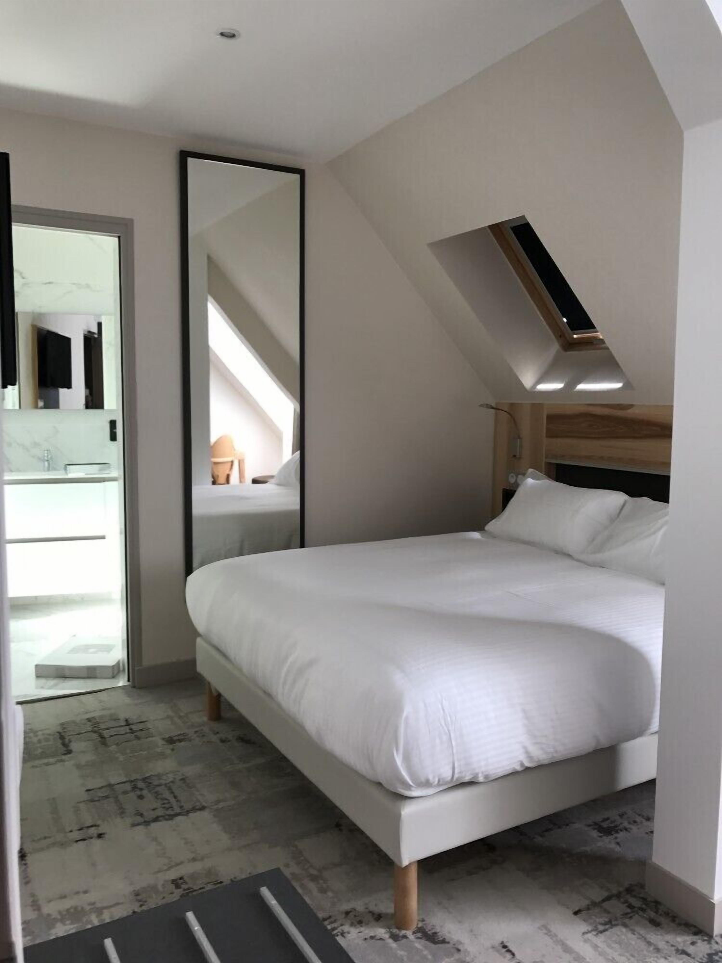Een moderne slaapkamer met een groot bed, dakraam, spiegel en een badkamer met een marmeren aanrecht.