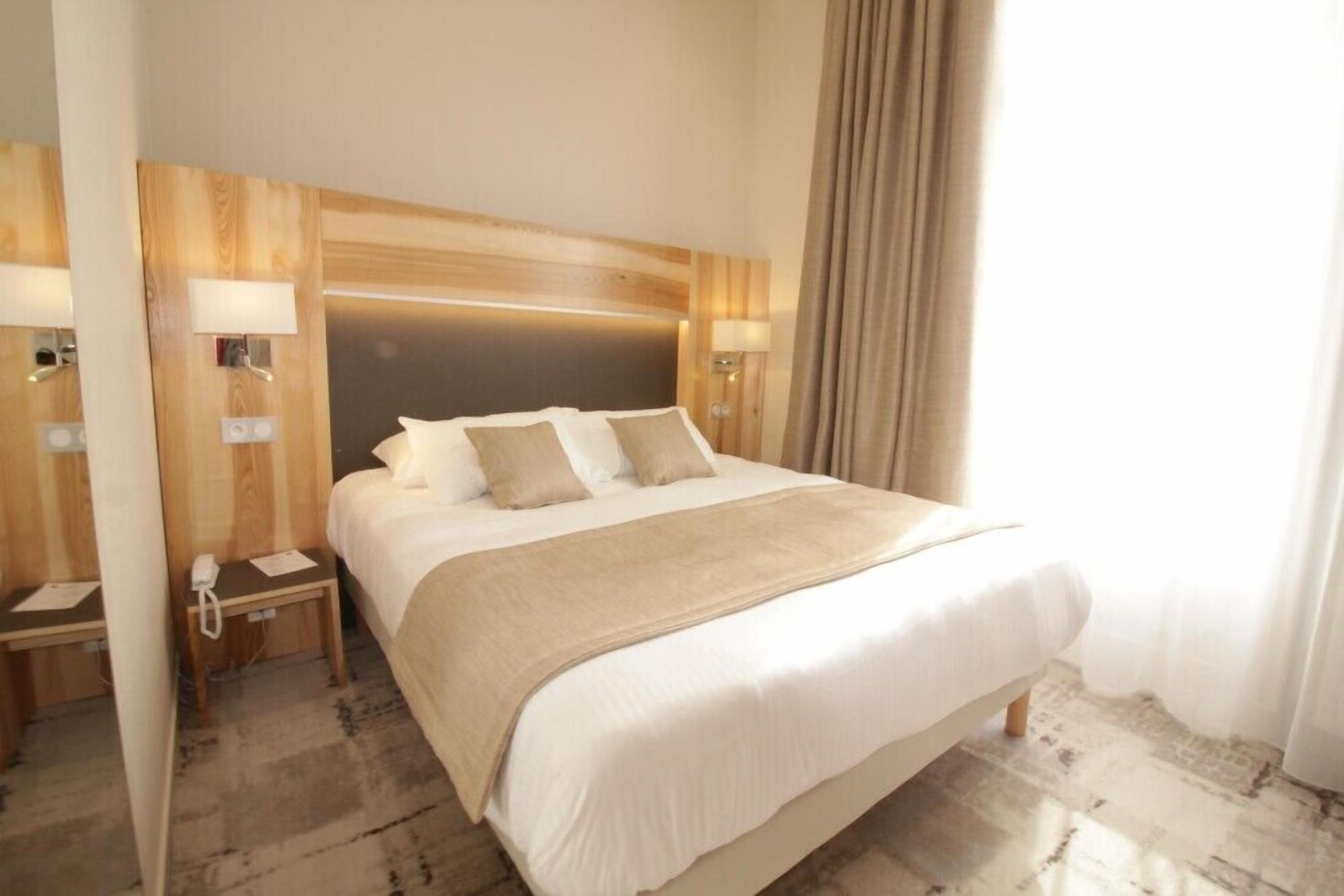 Une chambre d’hôtel avec un grand lit, une tête de lit en bois, des lampes de chevet et un téléphone sur une table de chevet.