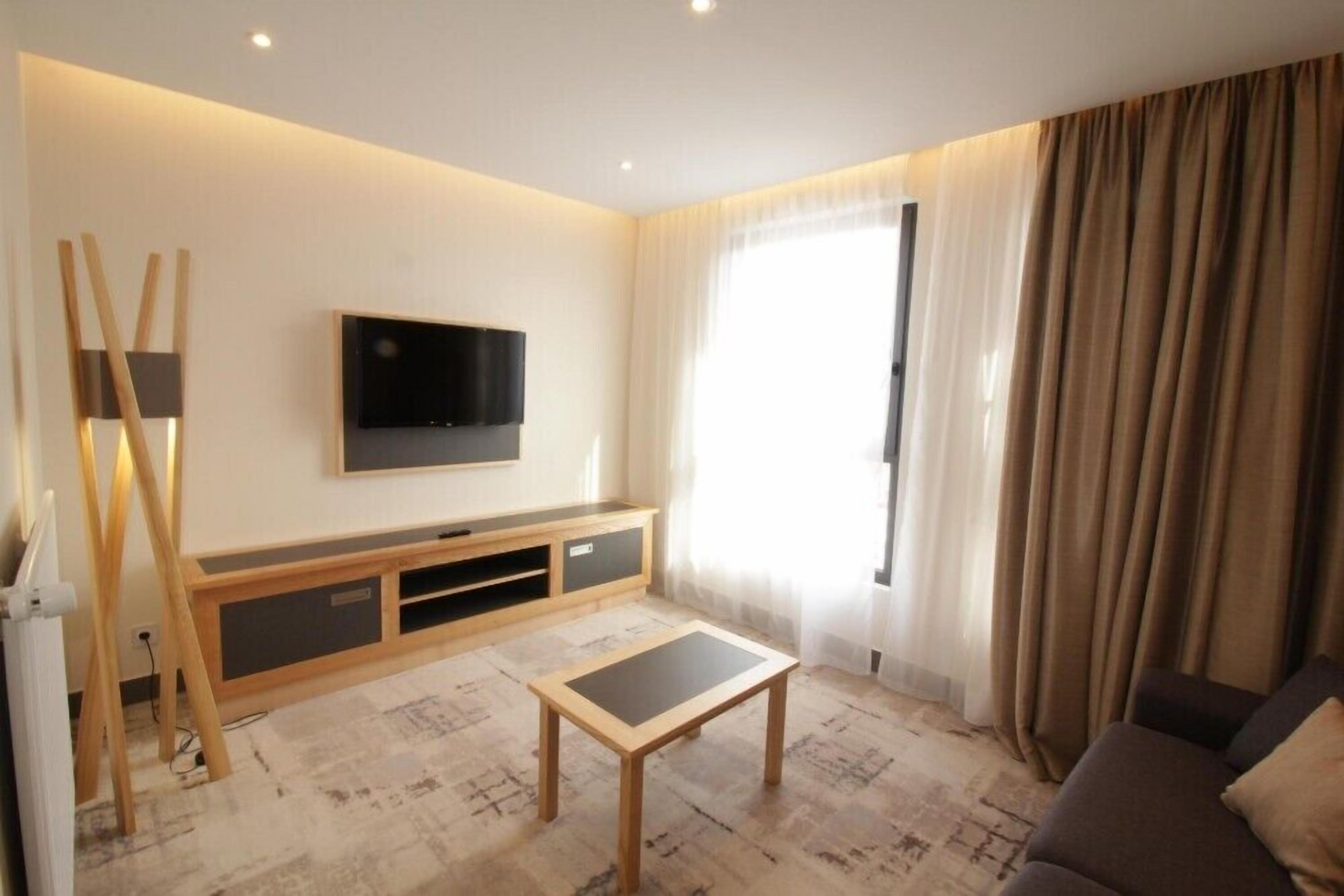 A modern living room with a flat-screen TV mounted on the wall, a wooden coffee table, and a sofa.