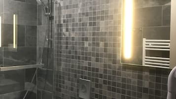 Un baño moderno con ducha envuelta en vidrio, un lavabo blanco y una pared con azulejos que incorpora un espejo.