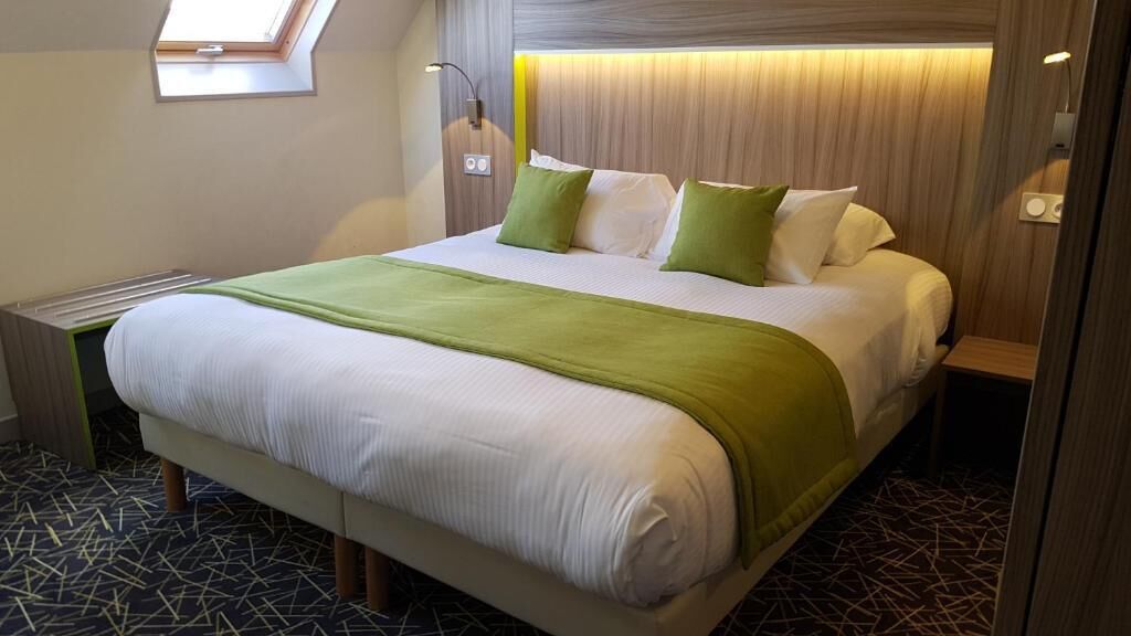 Un letto rifatto con cura, una coperta verde, un comodino e un tavolino notte con una lampada.