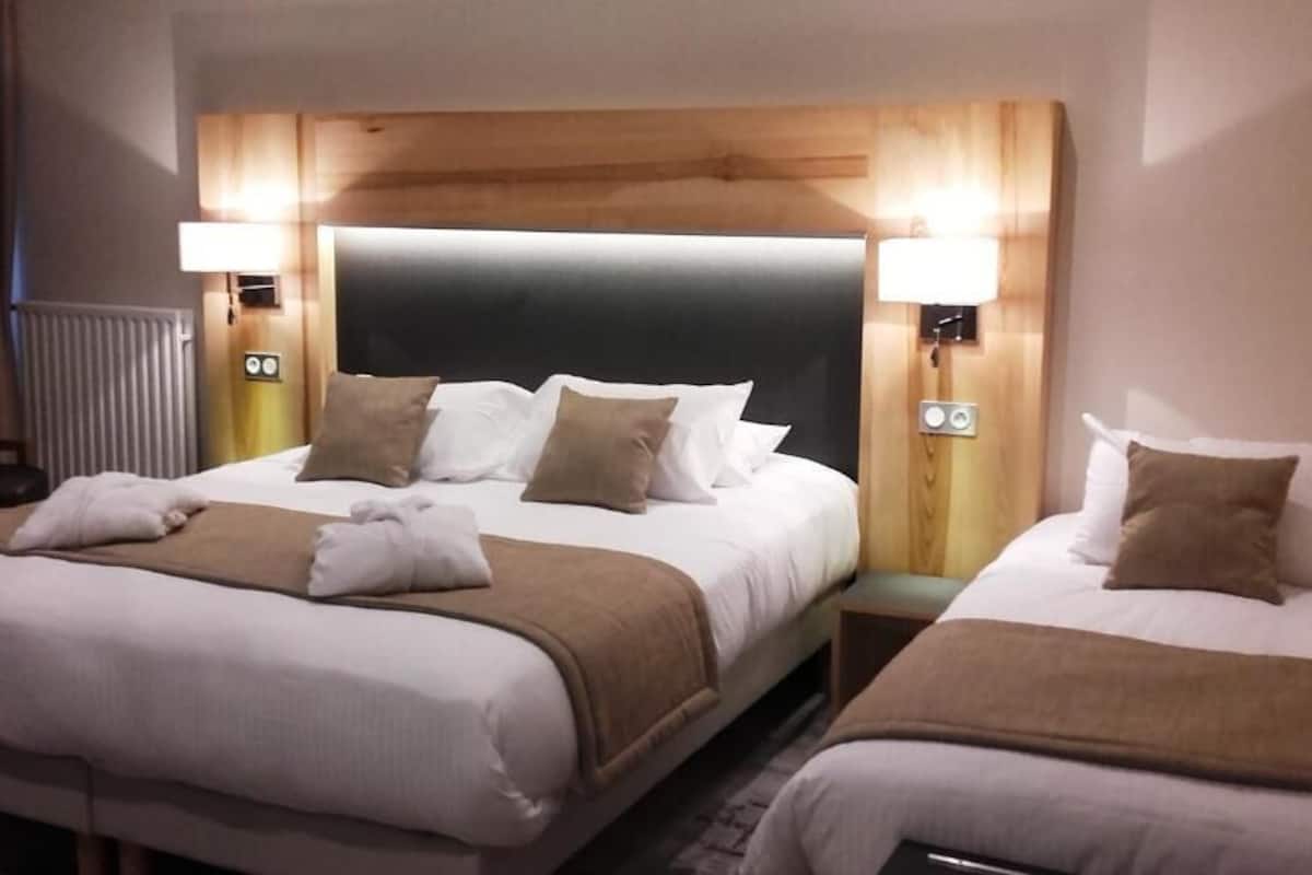 Quarto de hotel com duas camas, cada uma com cabeceira de madeira, roupa de cama branca e duas luminárias de cabeceira.