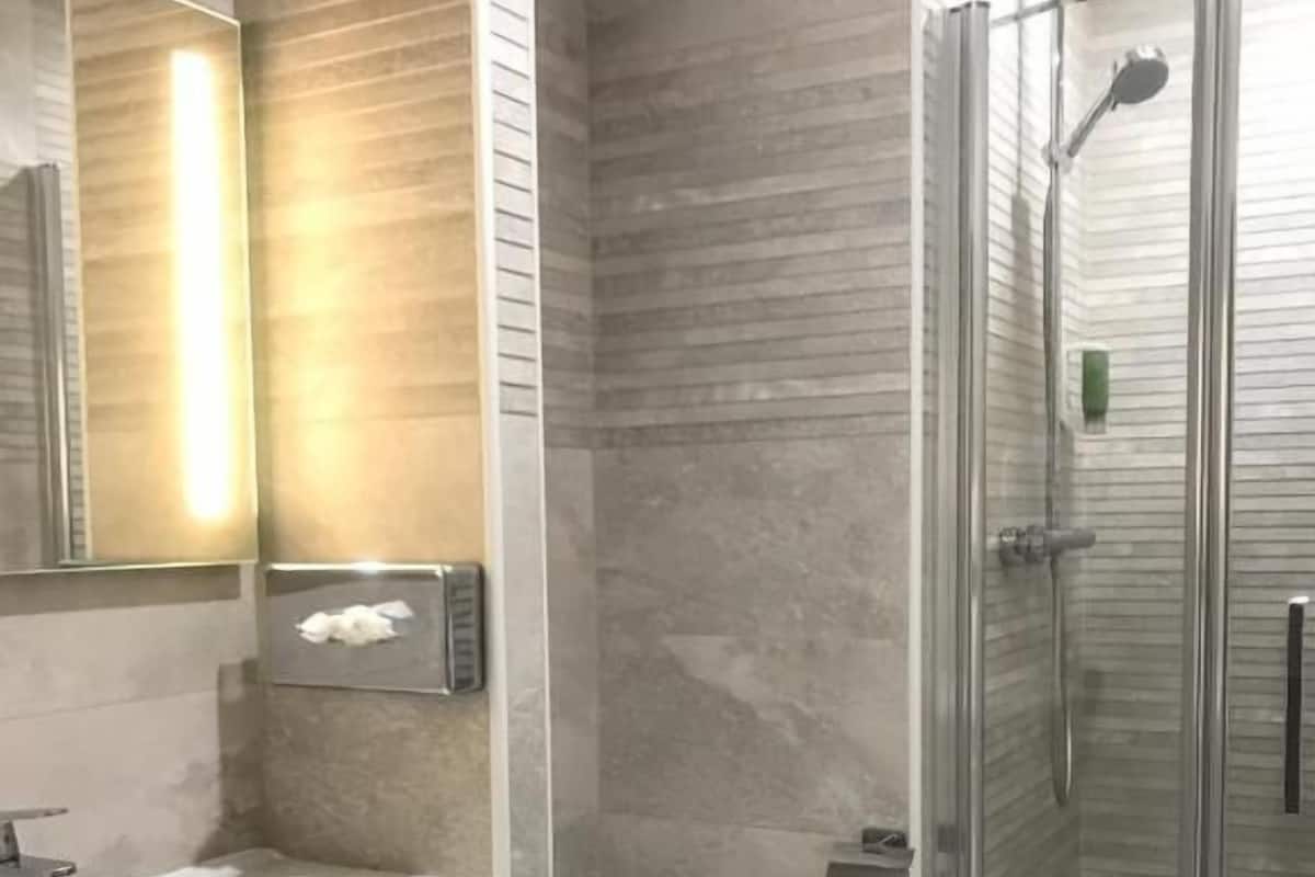 Casa de banho com lavatório branco, sanita e zona de duche com divisória de vidro.