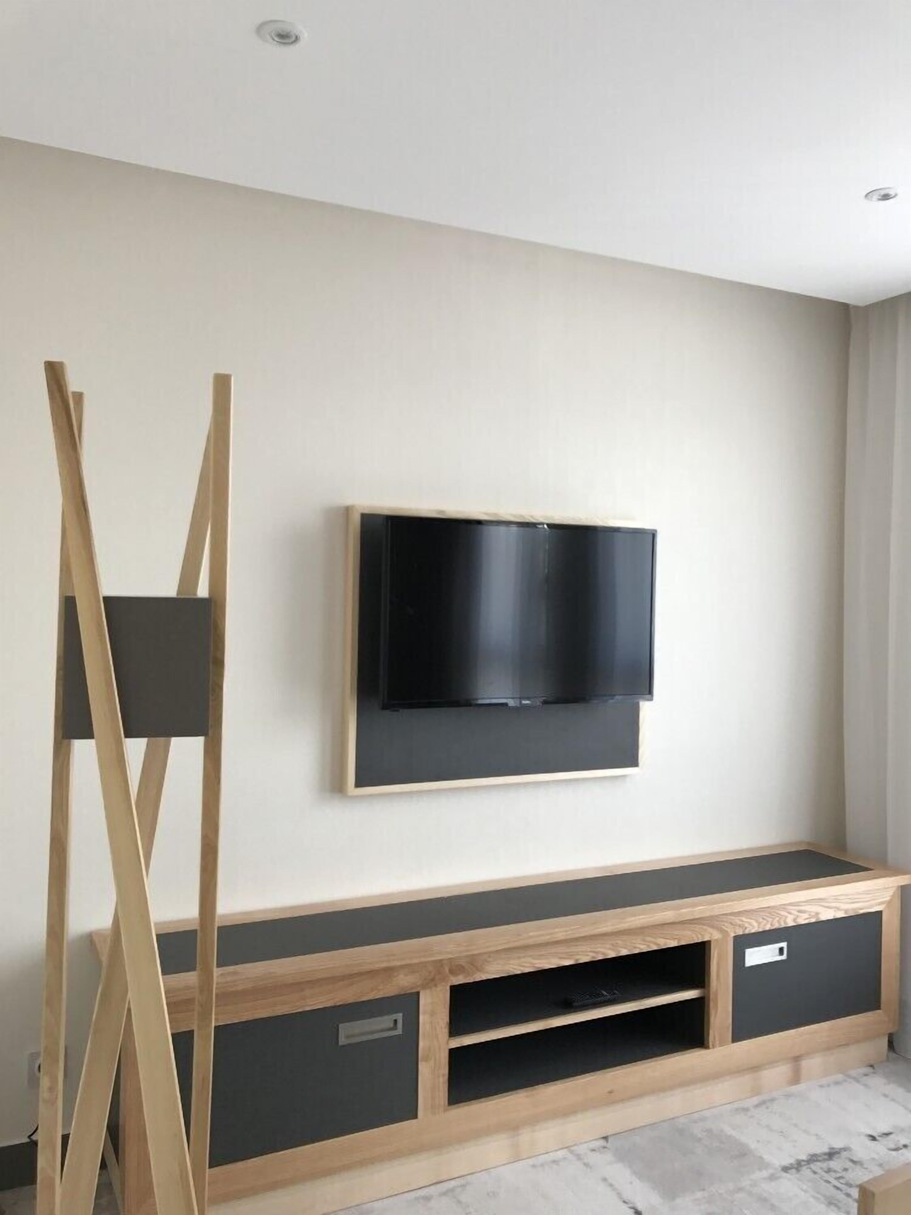Una sala moderna con un televisor de pantalla plana montado en la pared, un mueble de entretenimiento de madera debajo y una escalera de madera apoyada contra la pared.