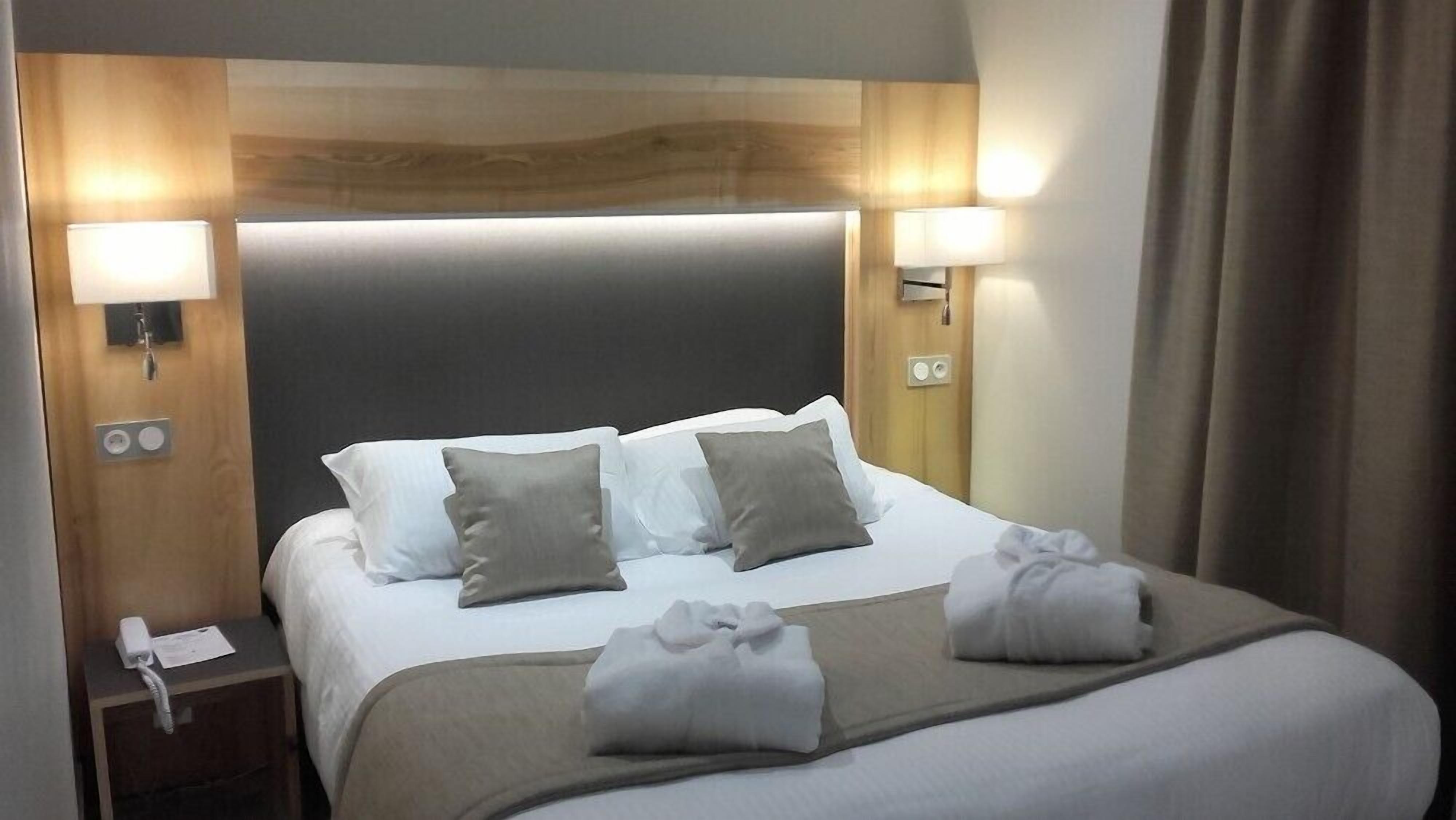 A hotel room with a large bed, two bedside lamps, a wooden headboard, and a telephone on the nightstand.