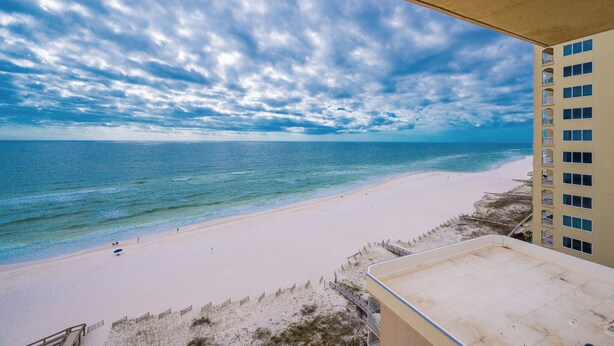 Vista de una playa desde un balcón con vista a una playa arenosa y al océano bajo un cielo parcialmente nublado.